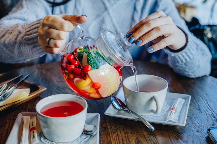 Woman Filling Tea In Cup On Table