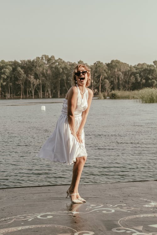 Blonde Woman Posing at a Waterfront in White Marilyn Monroe Dress