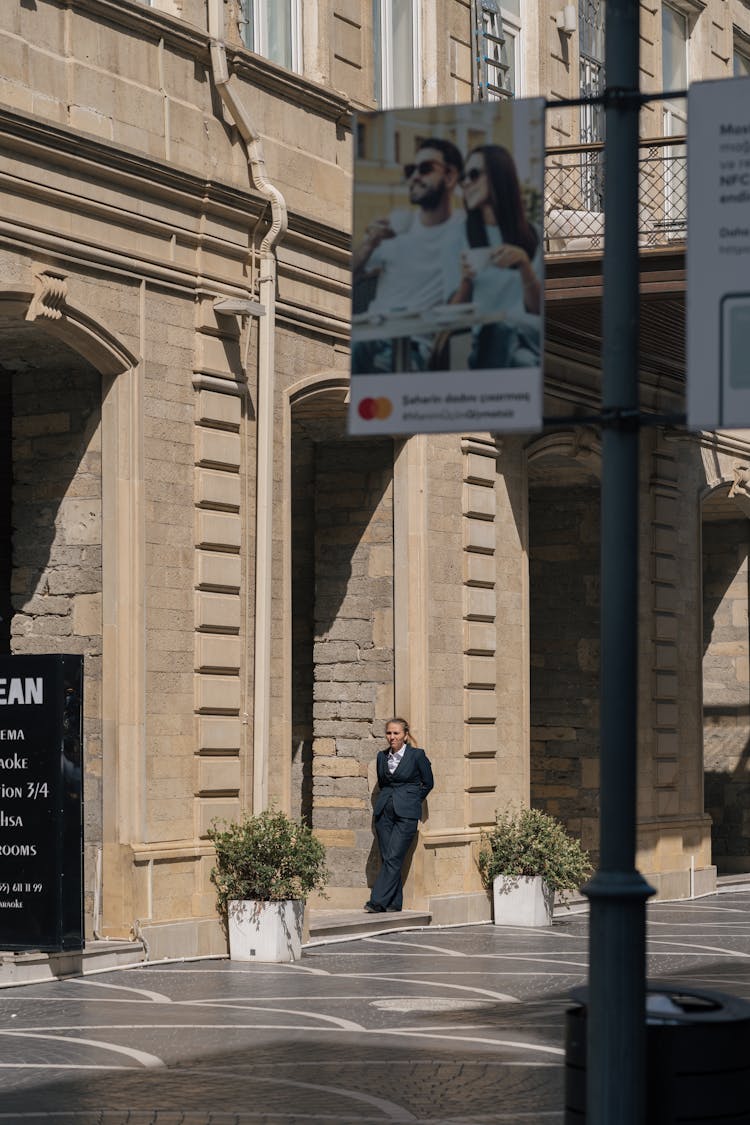 Woman In Black Suit Leaning On Building Wall On A City Street