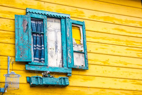 Free Rustic blue window with peeling paint on a vibrant yellow wooden house wall. Stock Photo