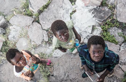 Three children standing on urban pavement in Lumeje, Angola, looking up. Top view shot with a Canon camera.