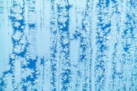 在明亮的蓝色背景下，窗户上霜冻图案的详细特写