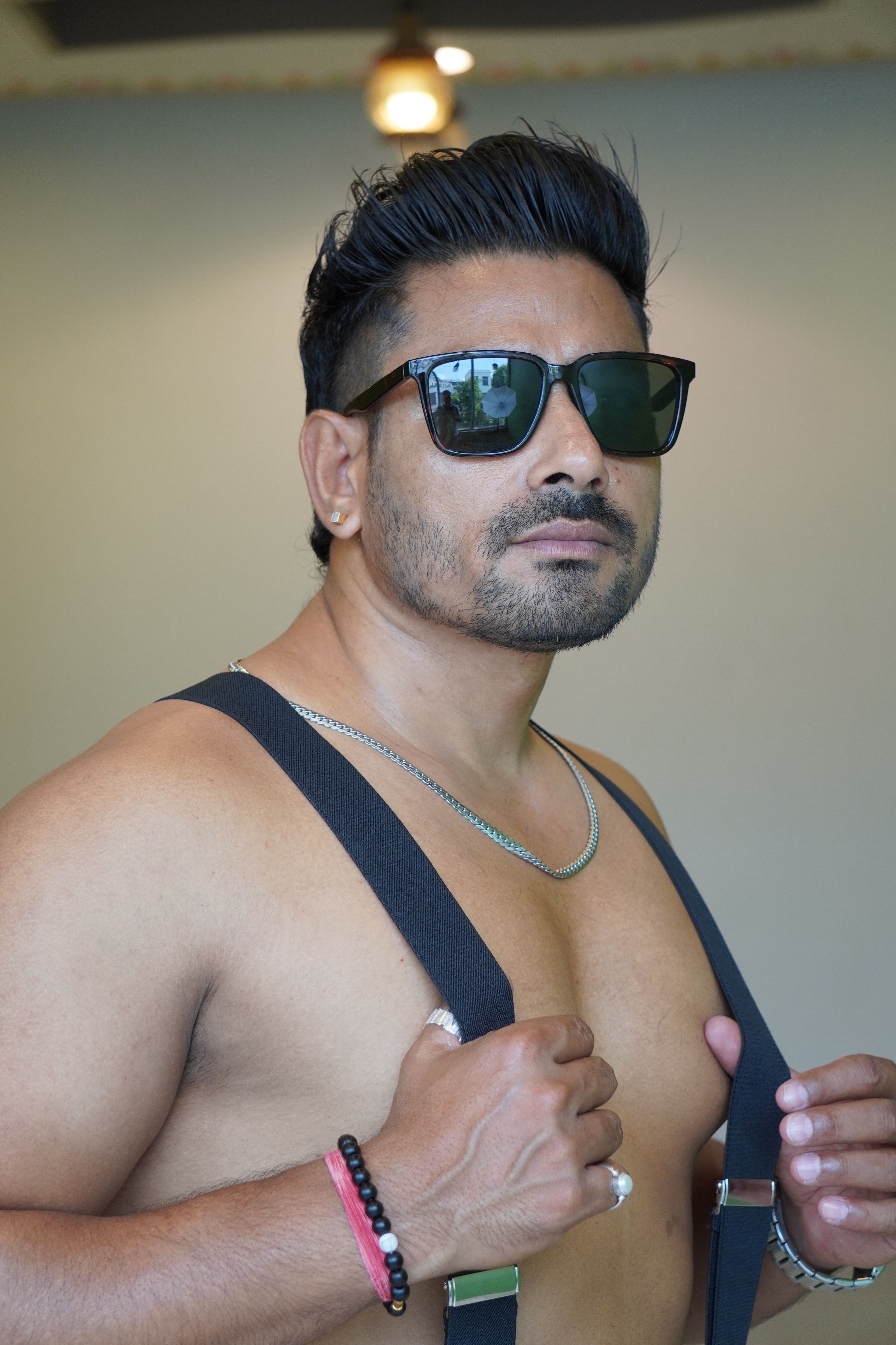 Muscular man with sunglasses poses confidently indoors, showcasing style and fitness.