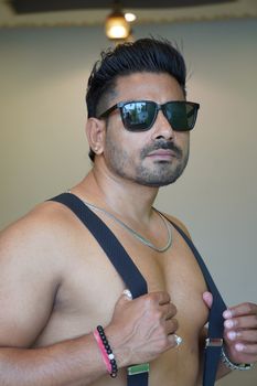 Muscular man with sunglasses poses confidently indoors, showcasing style and fitness.