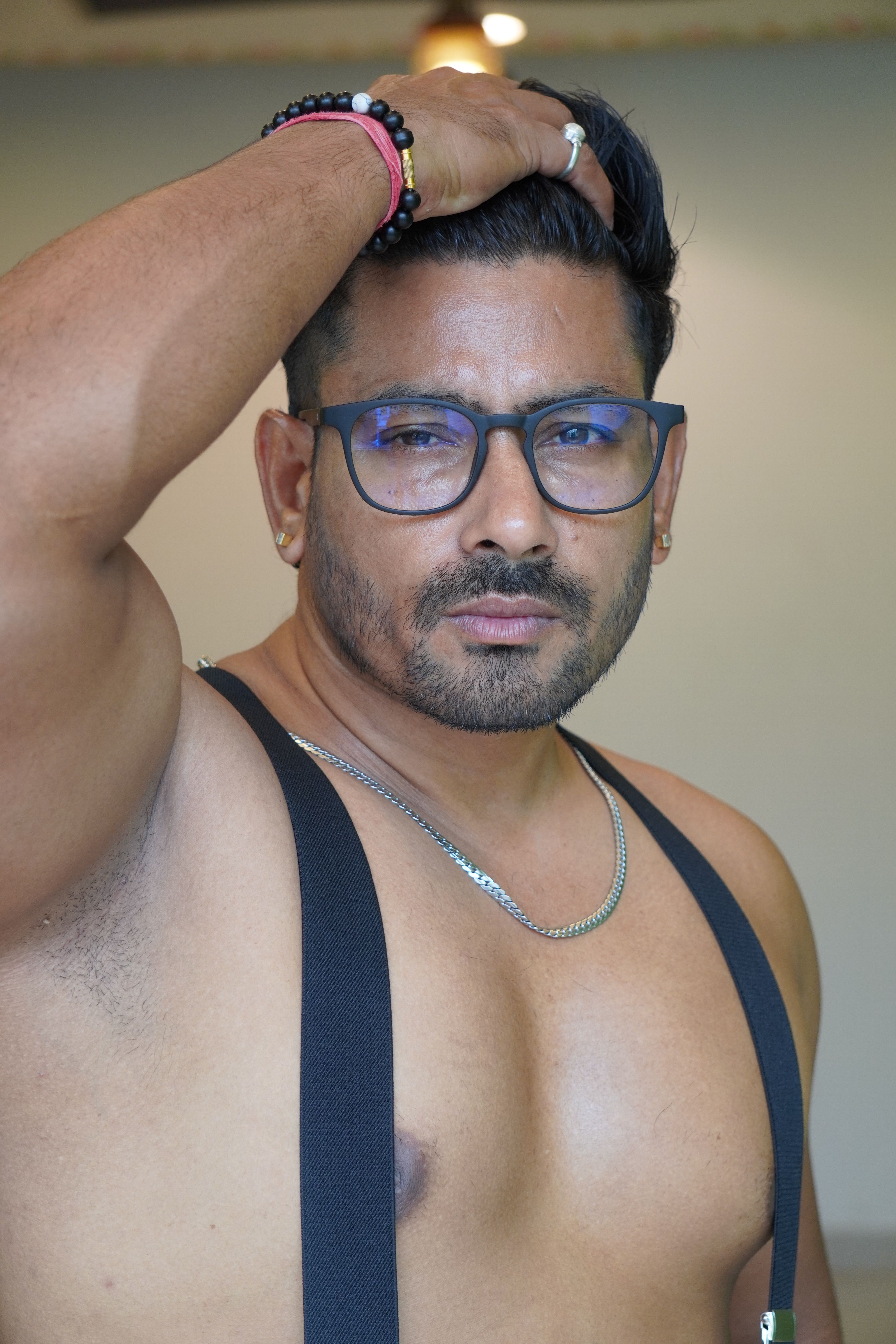 Portrait of a confident topless man with eyeglasses, necklace, and suspenders.