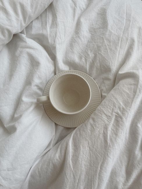 Top view of a white cup and plate on crumpled bedding, showcasing minimalism and calmness.