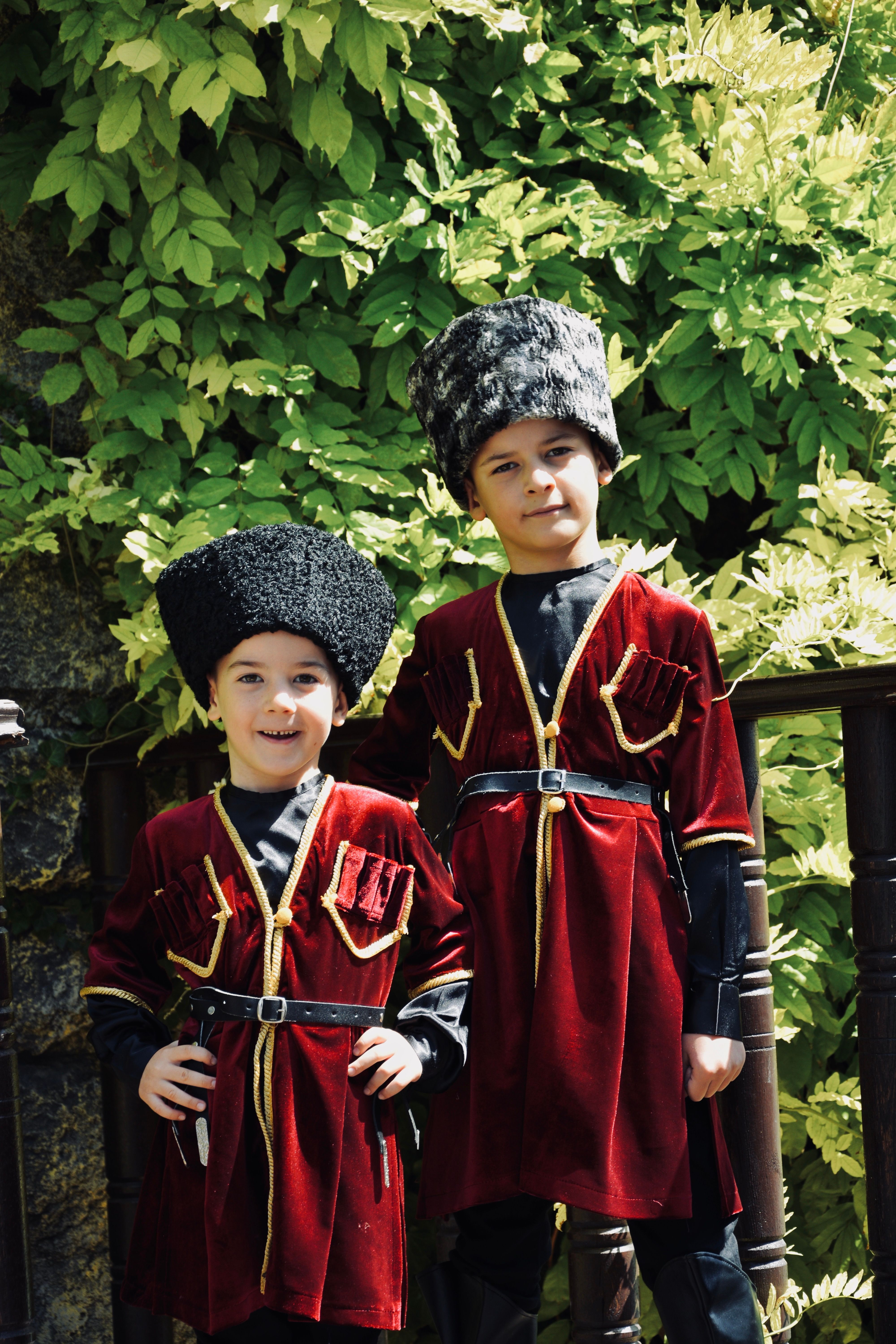 Two boys wearing traditional Caucasus costumes with fur hats standing outdoors.