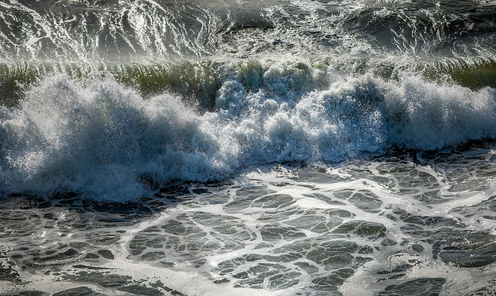 A powerful wave crashes on the shore, creating an impressive natural spectacle of sea foam and motion.