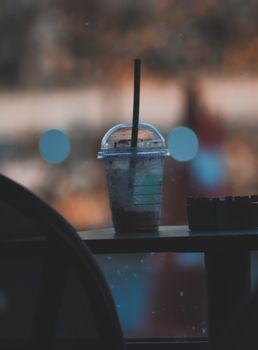 Chilled drink in disposable cup with straw on table with blurred background.