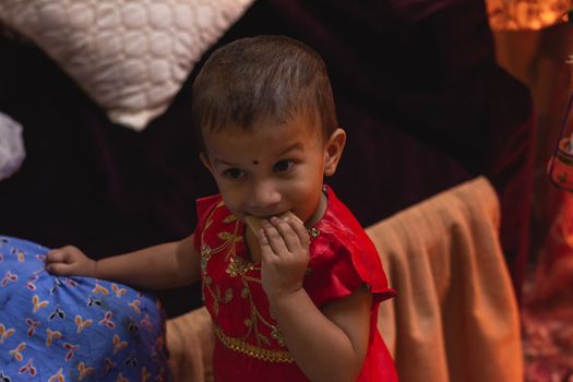 Adorable child in red traditional dress enjoying a snack indoors.