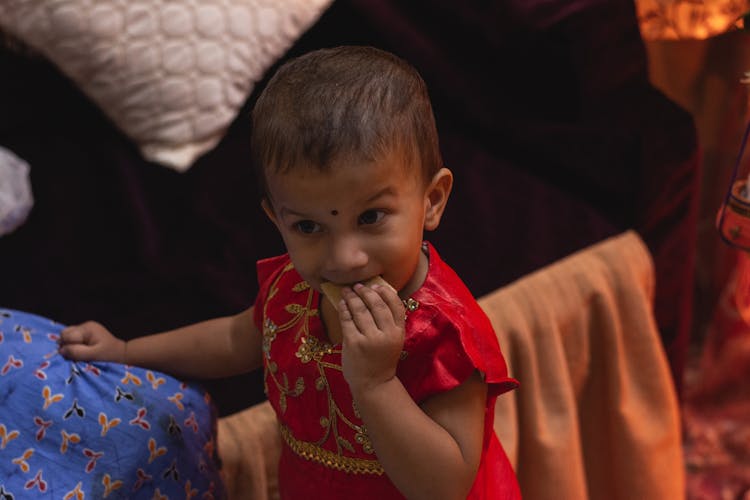 A Little Girl In A Traditional Dress Eating A Snack