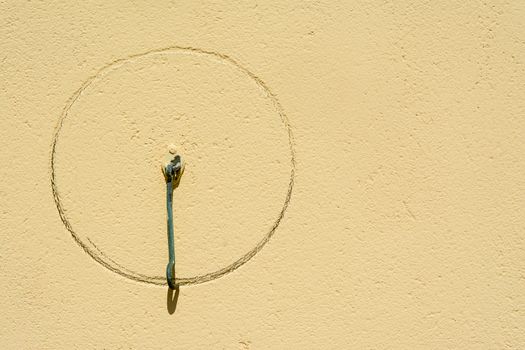 A solitary metal hook casting a shadow on a textured yellow wall in sunlight.