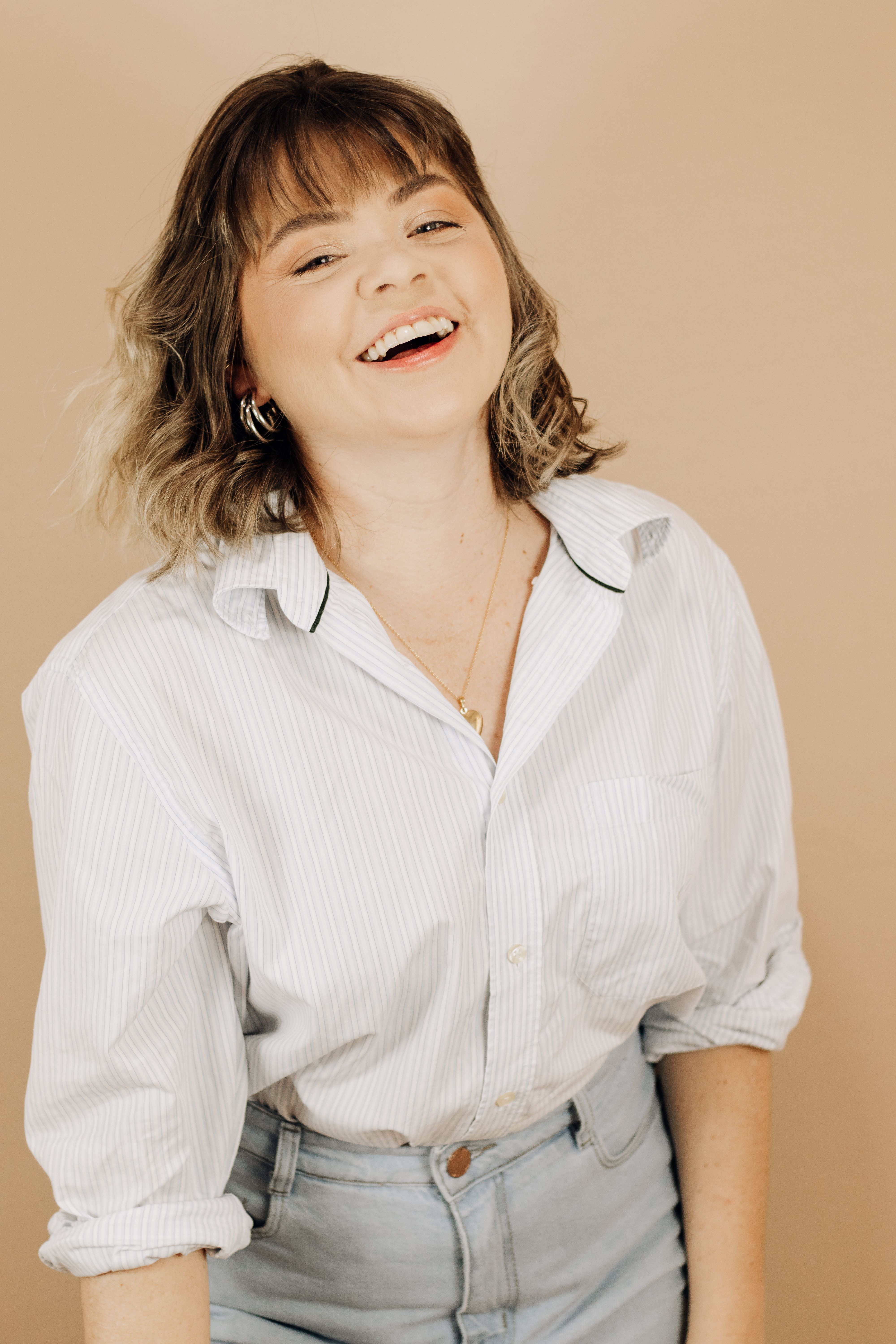 A joyful portrait of a young adult woman with brown hair in casual attire, set against a warm yellow background.