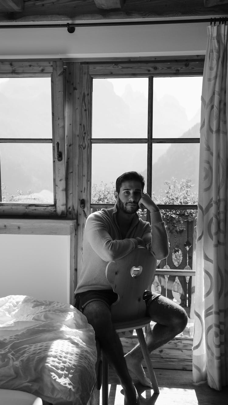 Man Sitting And Posing On Chair In Room In Black And White