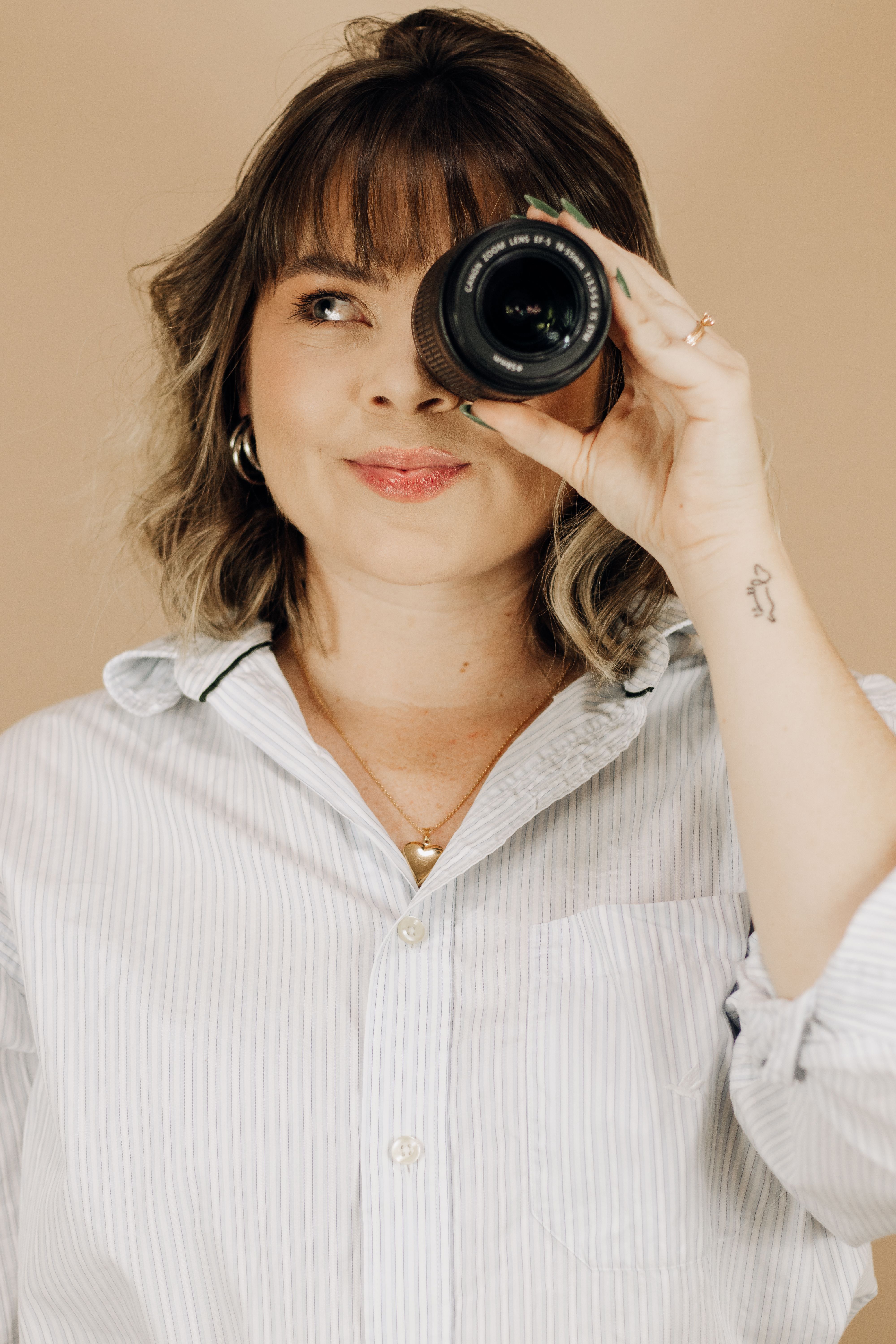 Studio portrait of a young woman holding a camera lens, expressing creativity and focus.