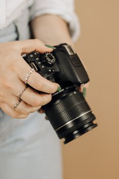 A woman with manicured nails holds a digital camera indoors for a close-up photography session.
