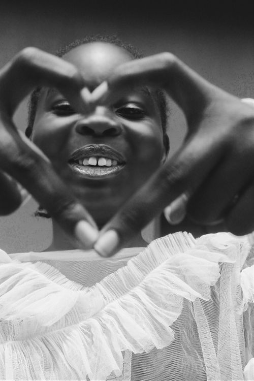 Free Black and white portrait of a young woman smiling, forming a heart with her hands. Stock Photo