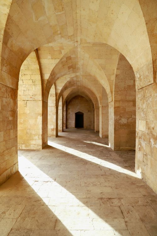 Free A serene stone colonnade with arches illuminated by sunlight, evoking a historic ambiance. Stock Photo