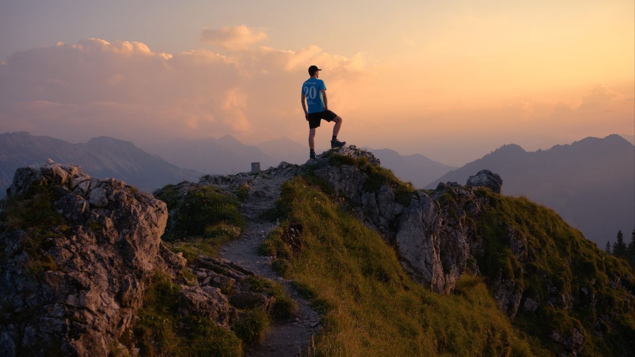 a lone hiker stands on a mountain peak admiring a breathtaking sunset