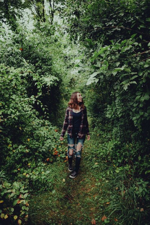Free A young woman in casual attire walks through a dense green forest, surrounded by nature. Stock Photo