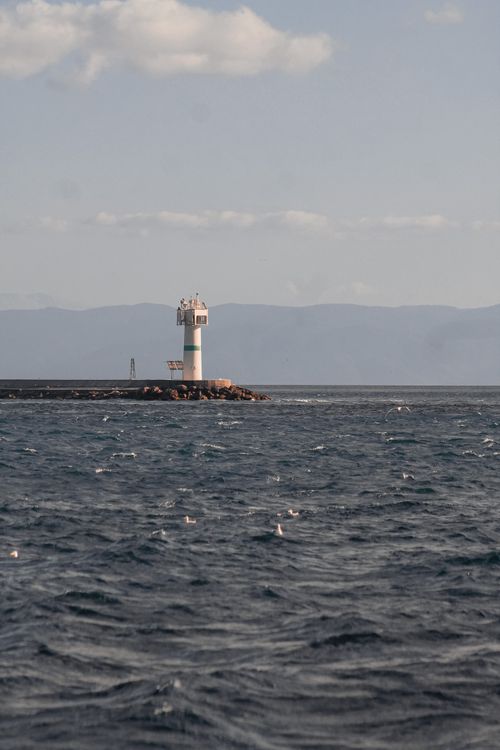 Free Calm seas surround a remote lighthouse on a rocky pier under a clear sky. Stock Photo