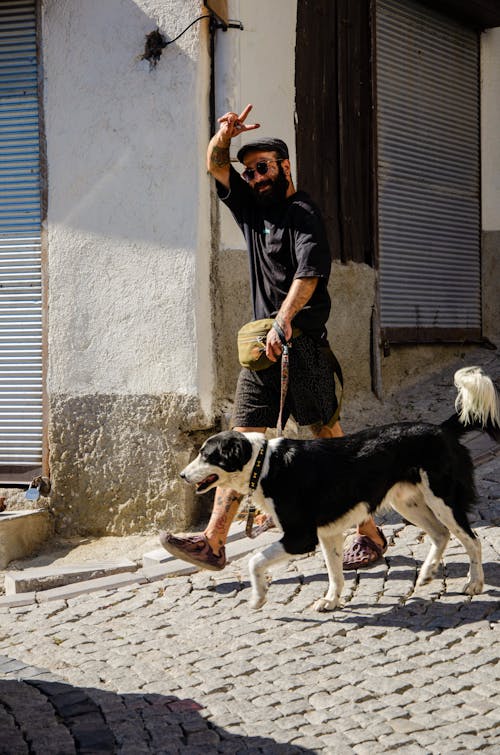 Bearded Man Walking a Dog Making a Peace Sign towards the Camera