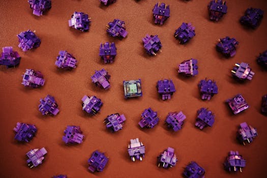 Flat lay of purple mechanical keyboard switches scattered on a brown surface.