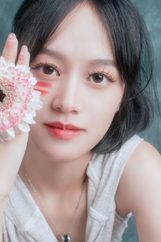 Close-up portrait of a woman holding a pink gerbera, showcasing beauty and elegance.