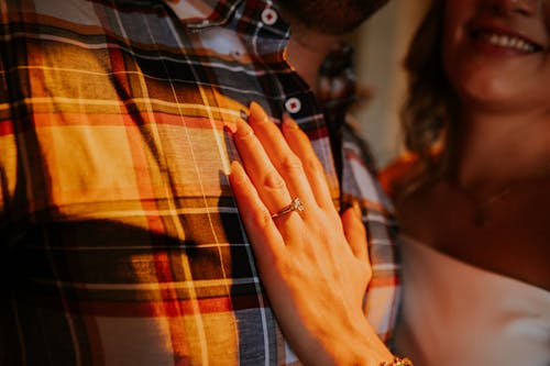 Hand of a Woman Wearing an Engagement Ring Touching the Torso of a Man Wearing a Plaid Shirt