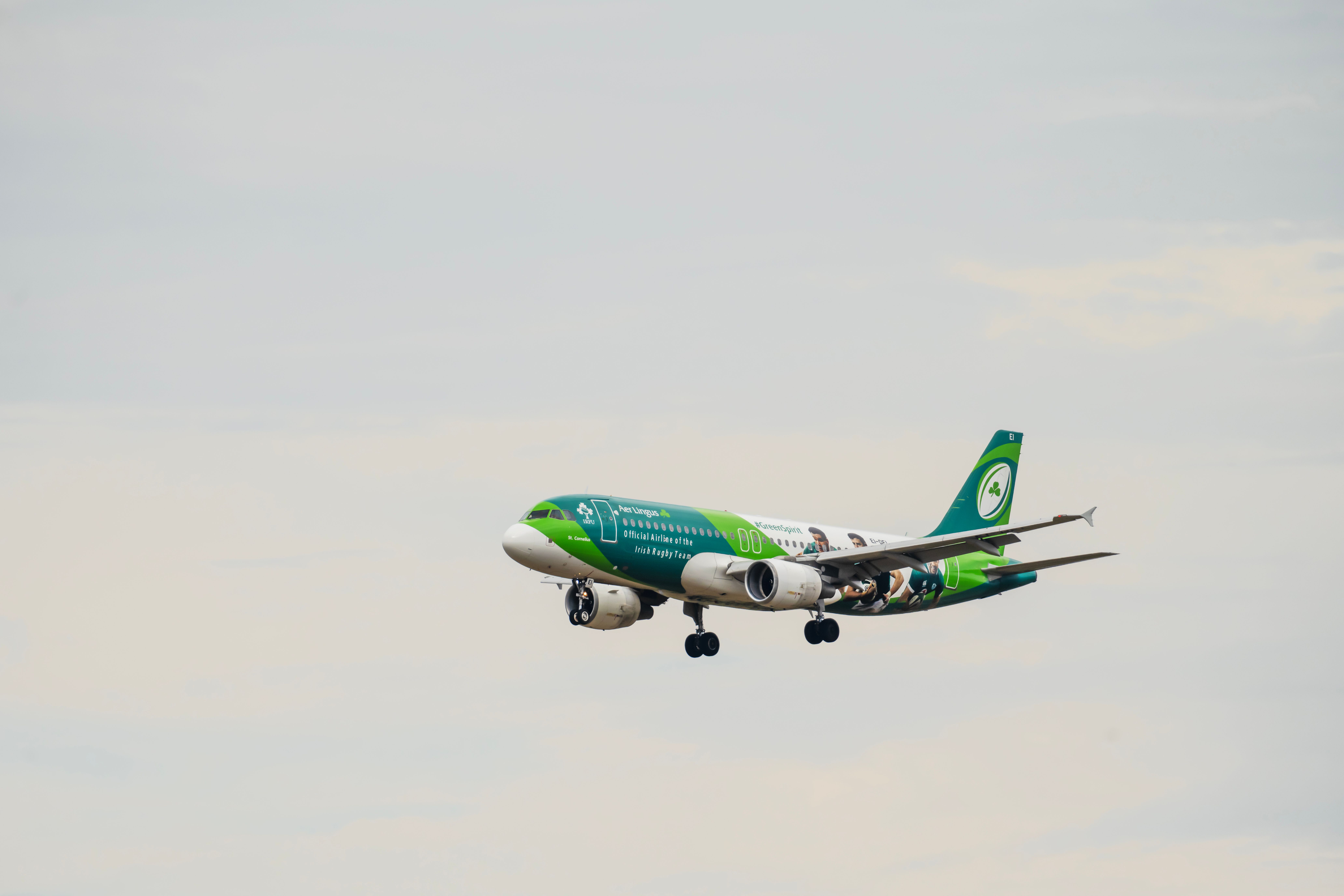 A green-liveried commercial airplane flying through an overcast sky, showcasing modern aviation.