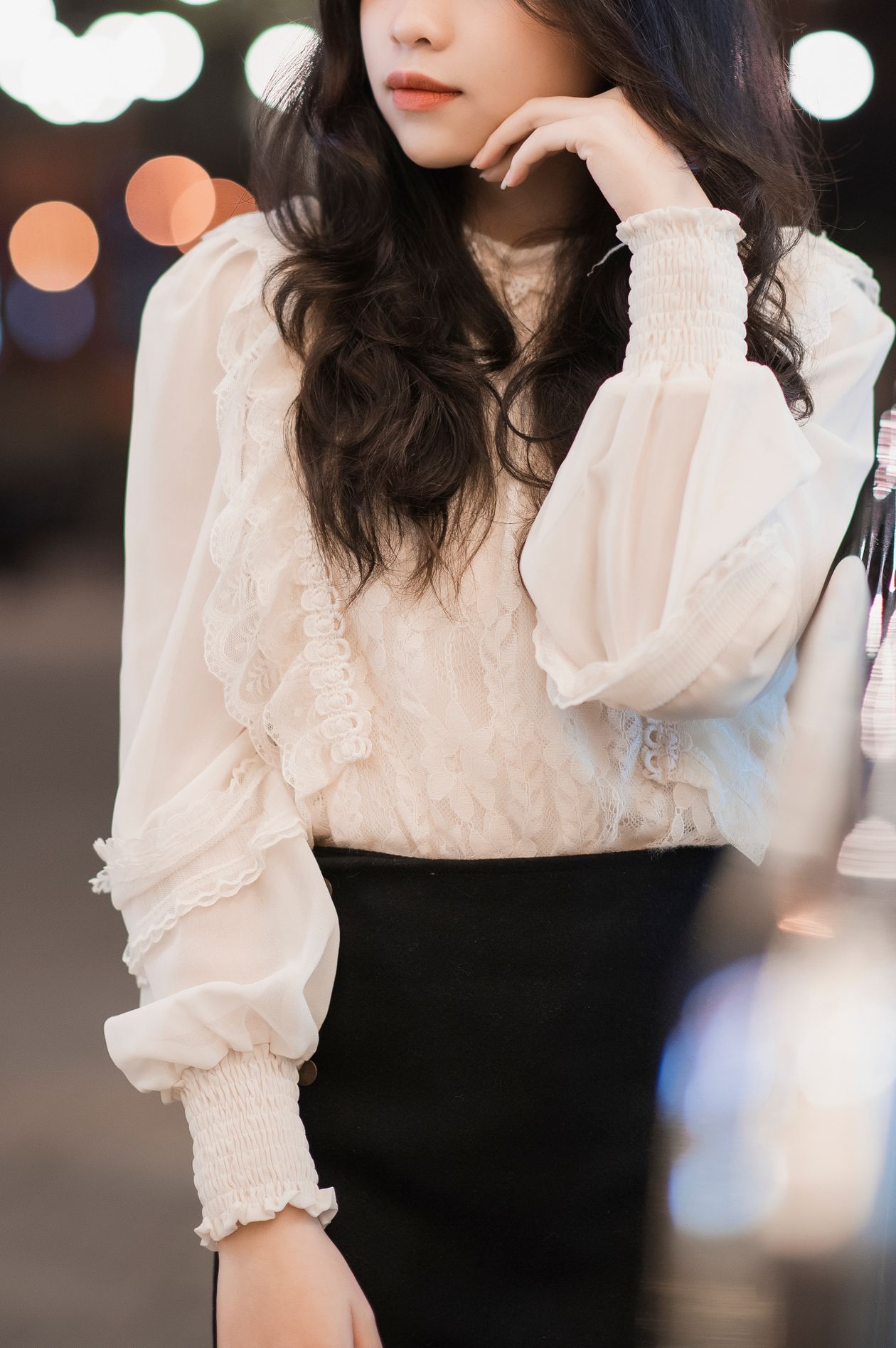 Woman in a white ruffle-front blouse with smocked cuffs and a black skirt