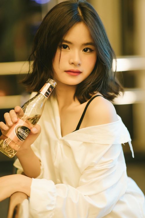 Free Asian woman in a white blouse holding a beer bottle, captured indoors. Stock Photo