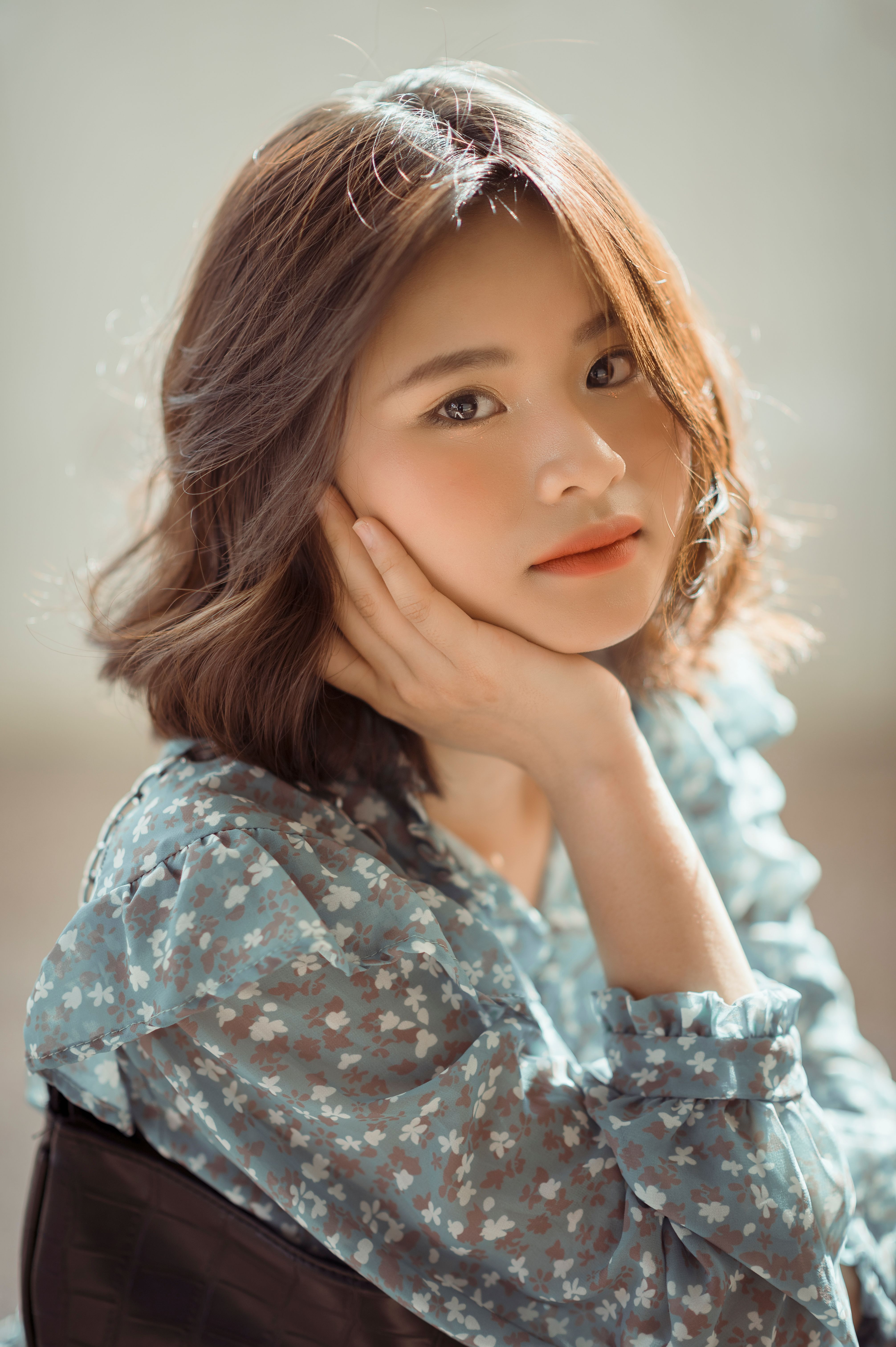 A young woman poses elegantly indoors wearing a floral blouse, exuding a serene and stylish mood.
