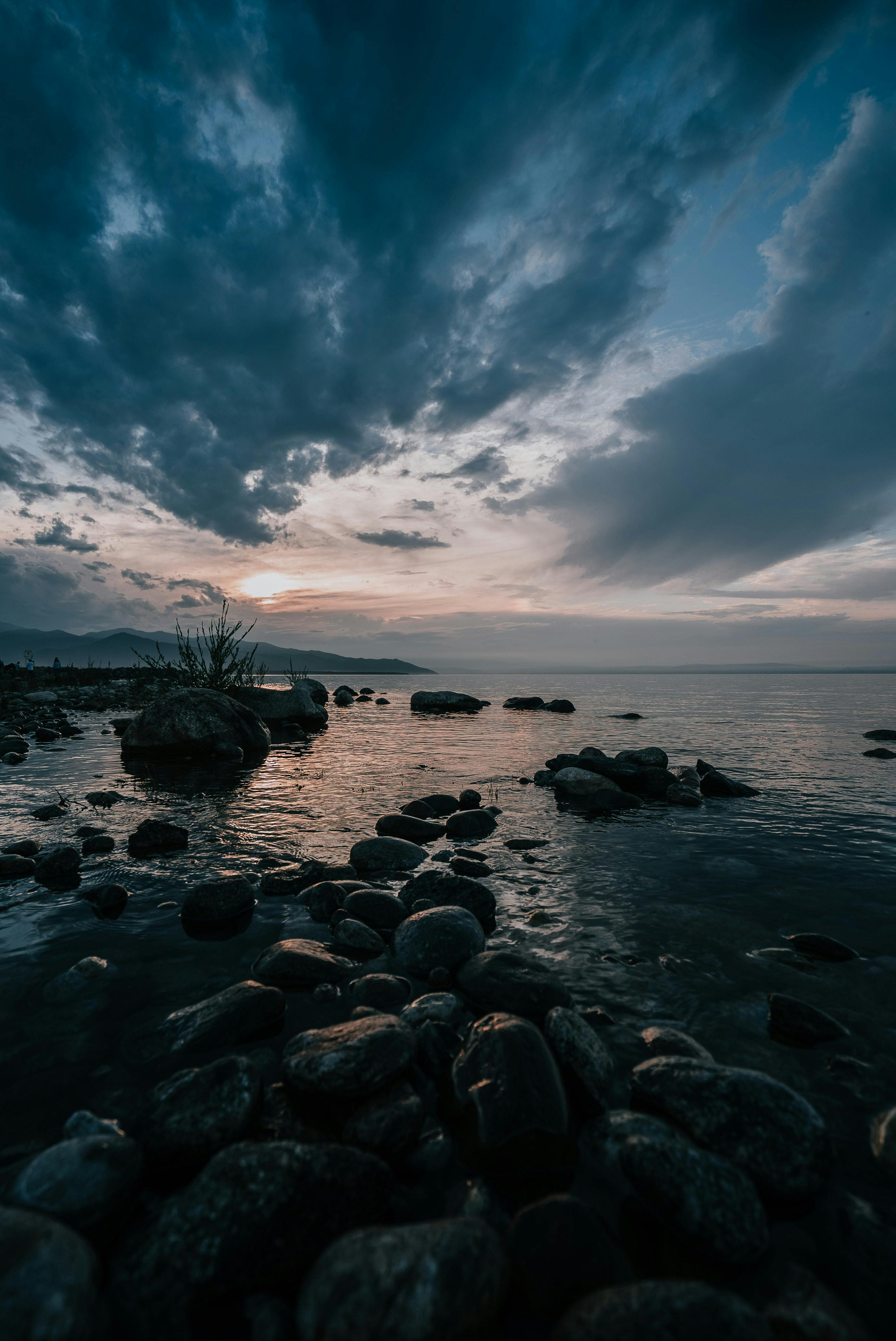 Serene coastline with rocks and dramatic clouds at twilight. Perfect for nature lovers and travelers.