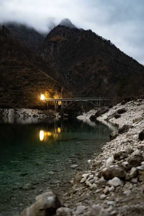Free A tranquil scene featuring a bridge illuminated by soft light, reflecting in a clear mountain lake. Stock Photo