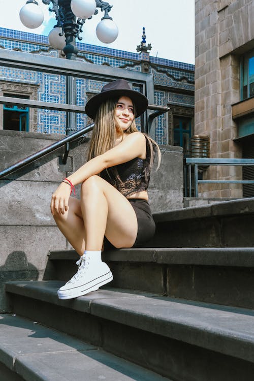 Young Woman in Black Fedora Hat, Lace Top and Shorts Sitting on Steps 