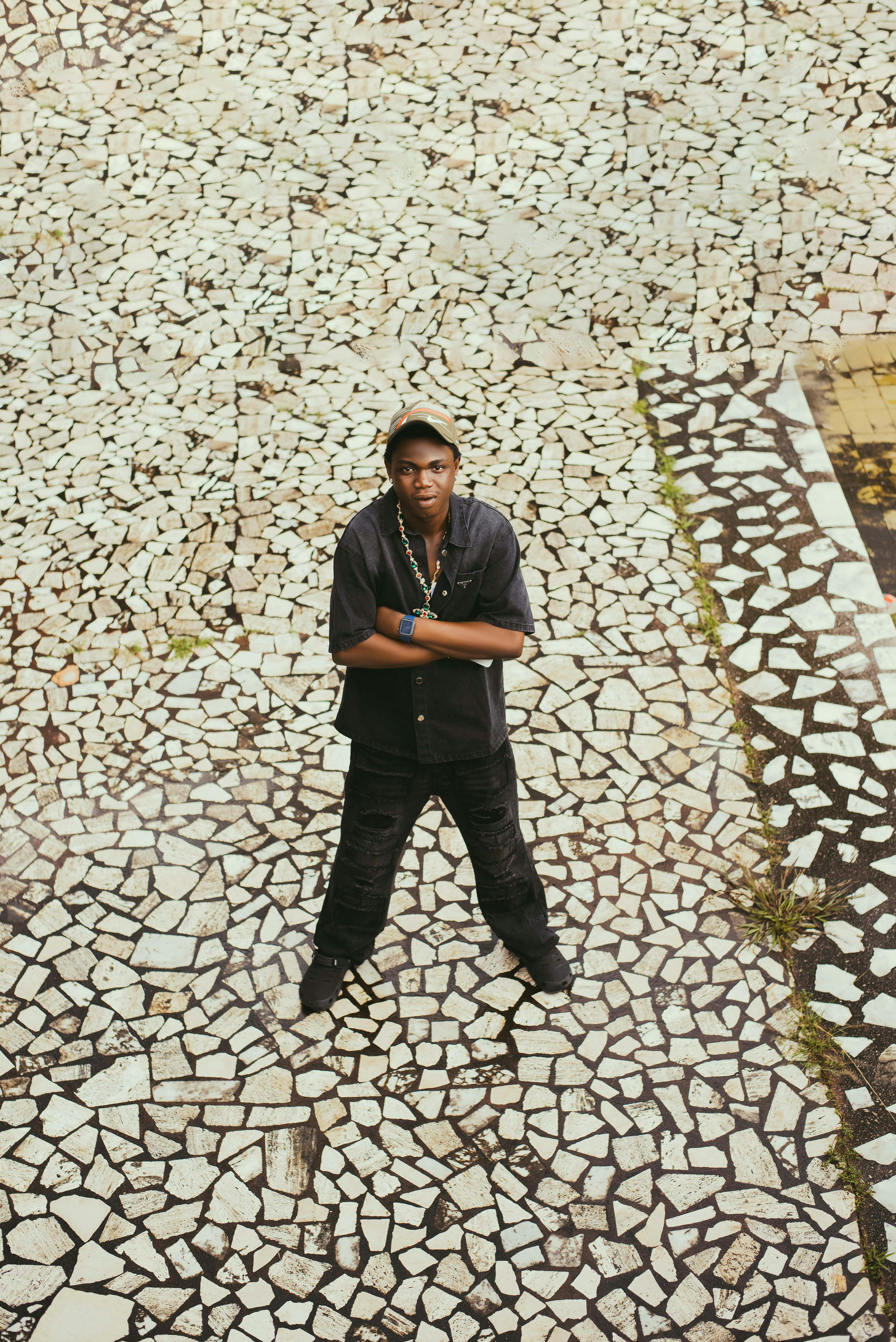 Stylish young man standing on mosaic pavement, arms crossed, in a high-angle shot.