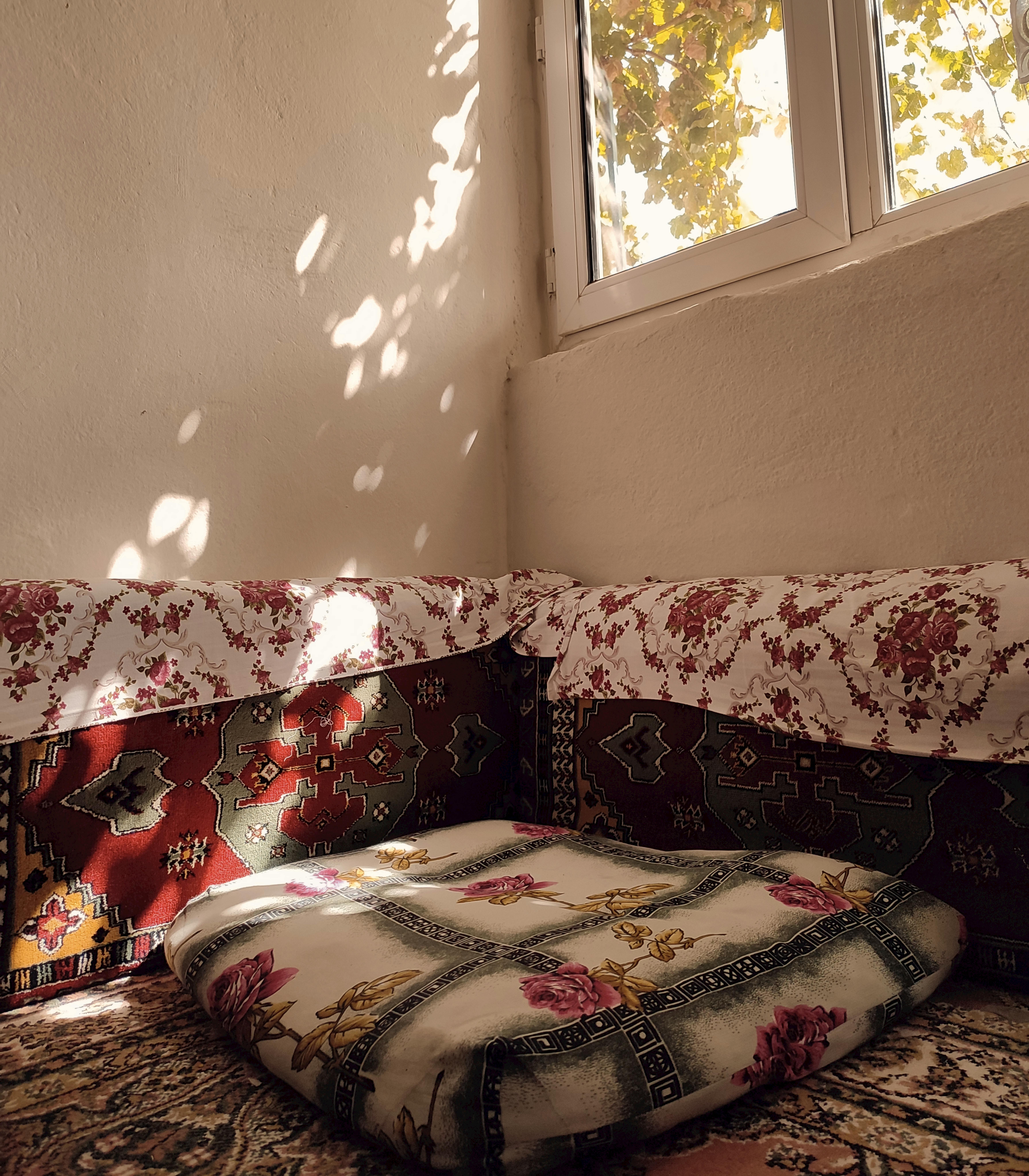 A sunlit room corner with vintage textiles and decorative pillows creating a cozy atmosphere.