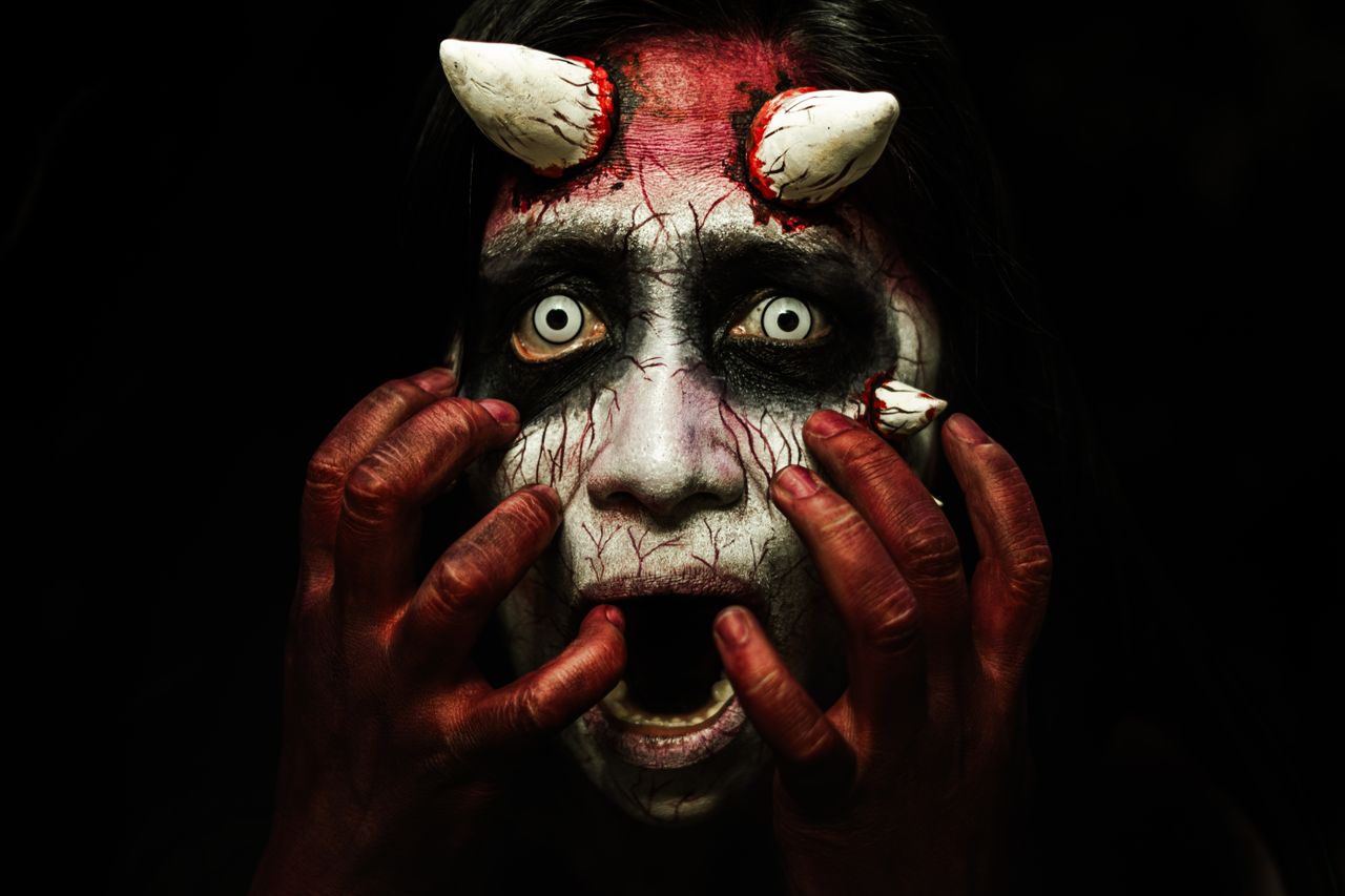 close up of an eerie demon character with elaborate face makeup and ho