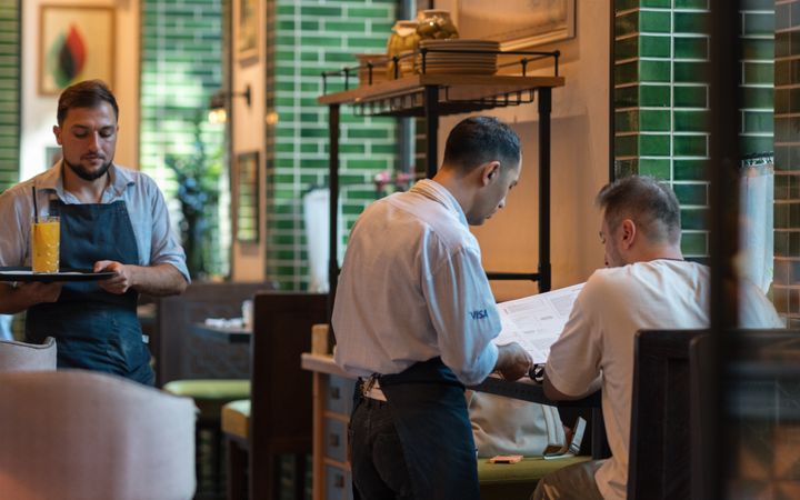 Waitstaff serving a customer in a modern restaurant with green tile decor.