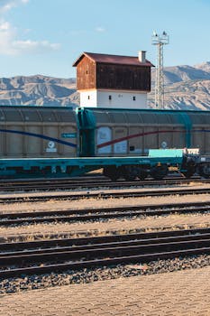 Cargo train stationed on railway tracks against scenic mountain backdrop under clear sky.