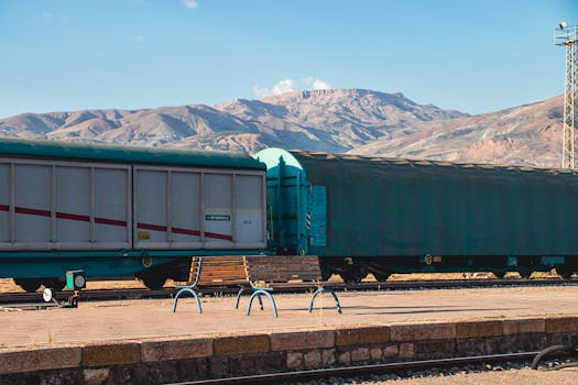 Freight train at a station with mountain backdrop under clear sky.