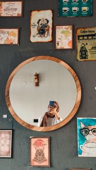 A woman capturing her reflection in a round mirror surrounded by artistic wall decor.