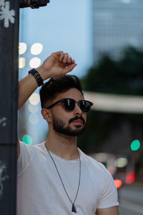 Free Man wearing sunglasses and white t-shirt posed against urban backdrop with city lights. Stock Photo