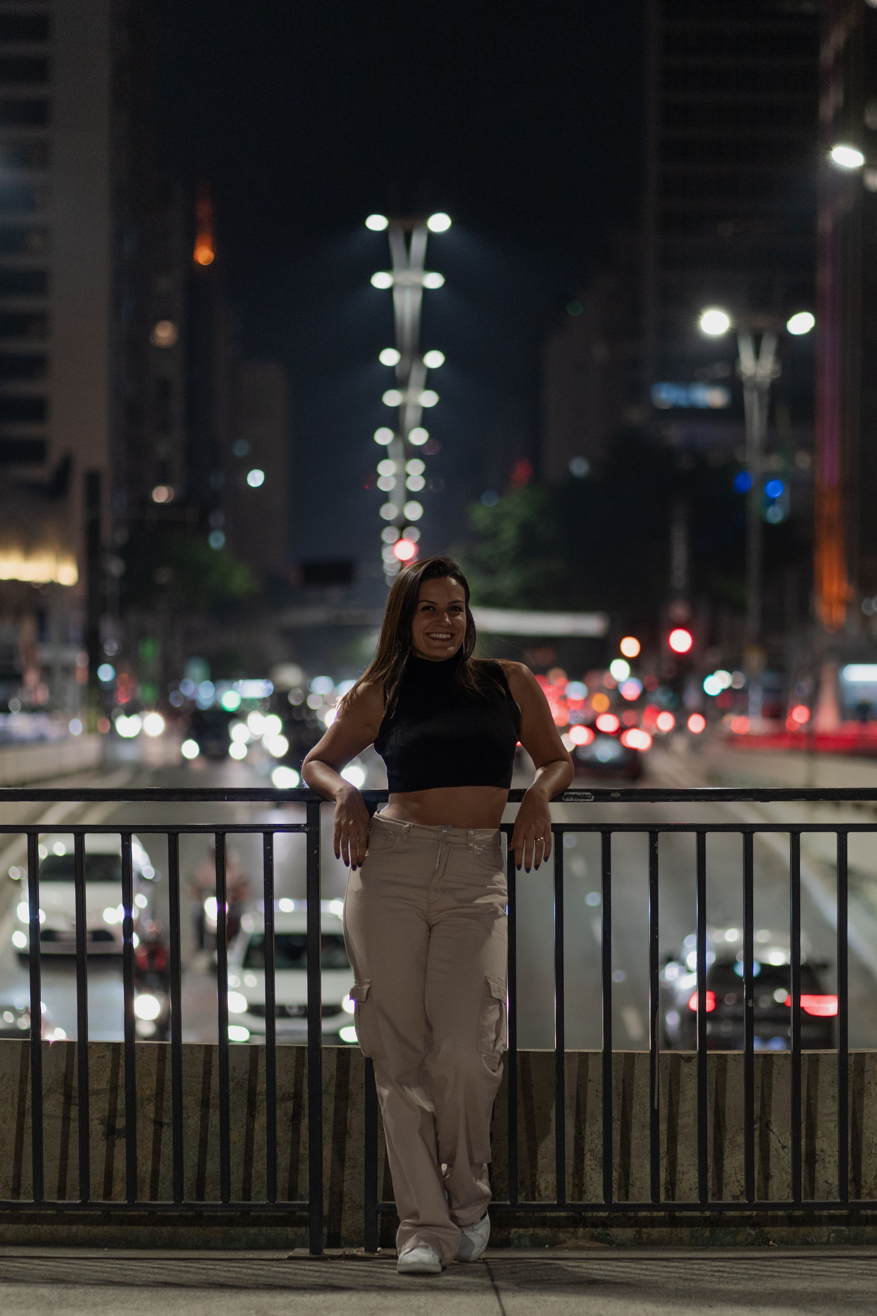 A stylish woman in a turtleneck top poses against a bustling city night backdrop.