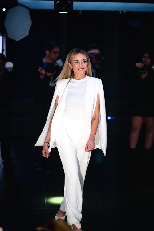 Free Blonde woman in elegant white suit smiles while walking on a fashion show runway. Stock Photo