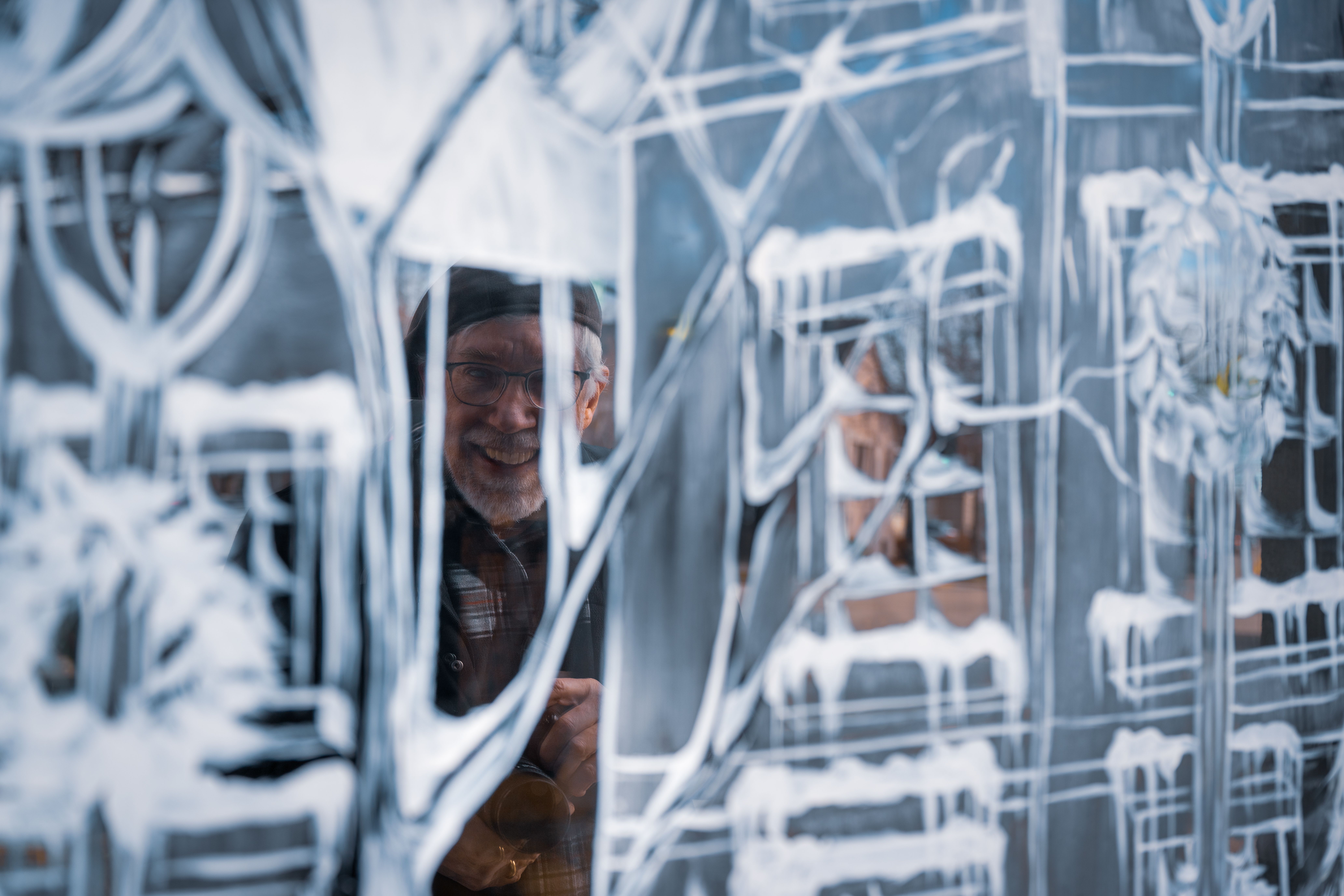 Elderly man smiling behind a frosted glass, creating an artistic and wintery scene.
