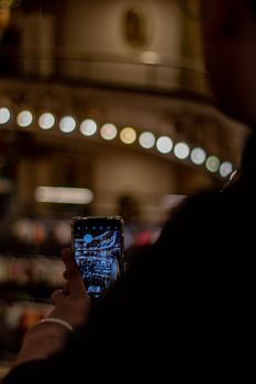 Close-up of a person photographing a brightly lit shopping mall interior on a smartphone.