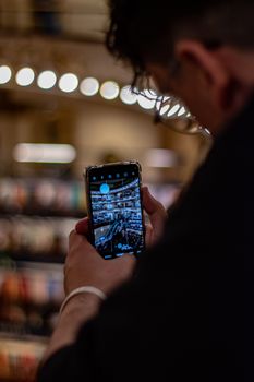 A man captures a shopping mall interior on his smartphone using selective focus.