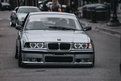 Free A stylish BMW E36 drives down an urban street, capturing city life and automotive elegance. Stock Photo